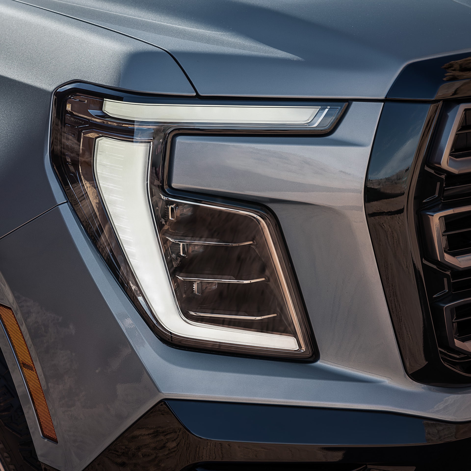 Close-up of the Illuminated LED Headlight and Daytime Running Lights of a Gray 2027 GMC Yukon Denali