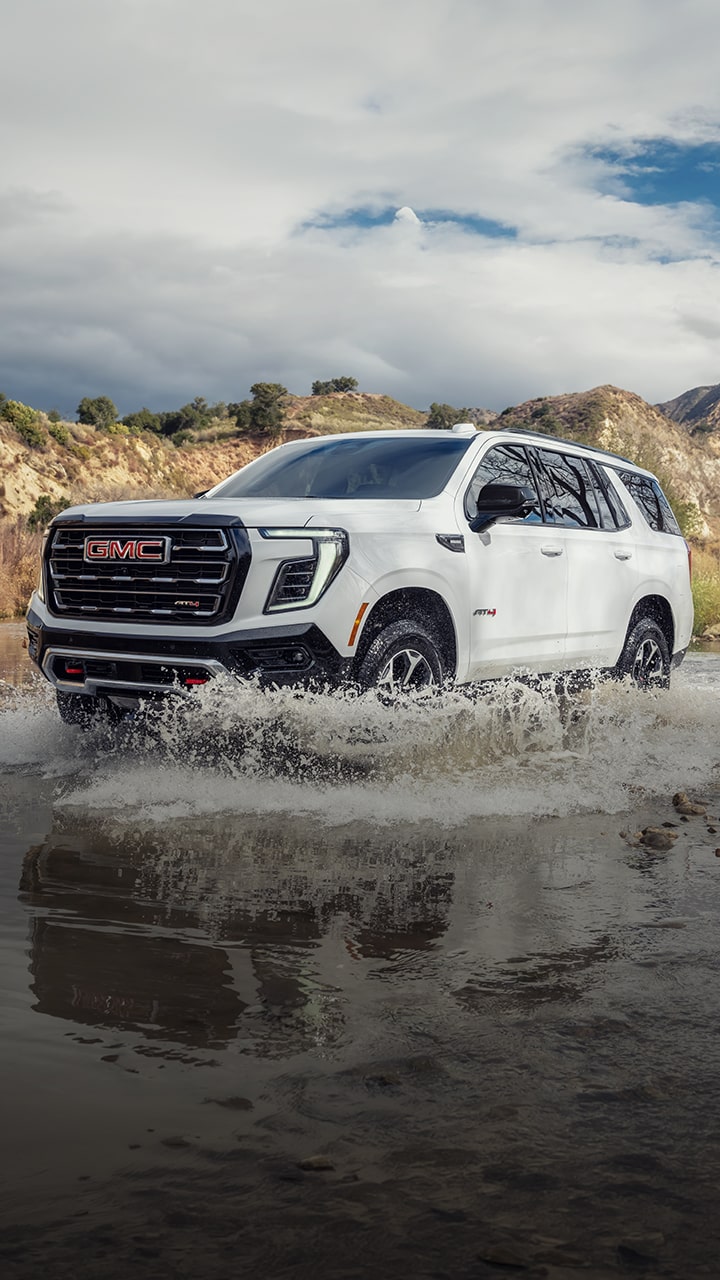 A White GMC Yukon AT4 Splashing Through Water on an Off-Road Trail