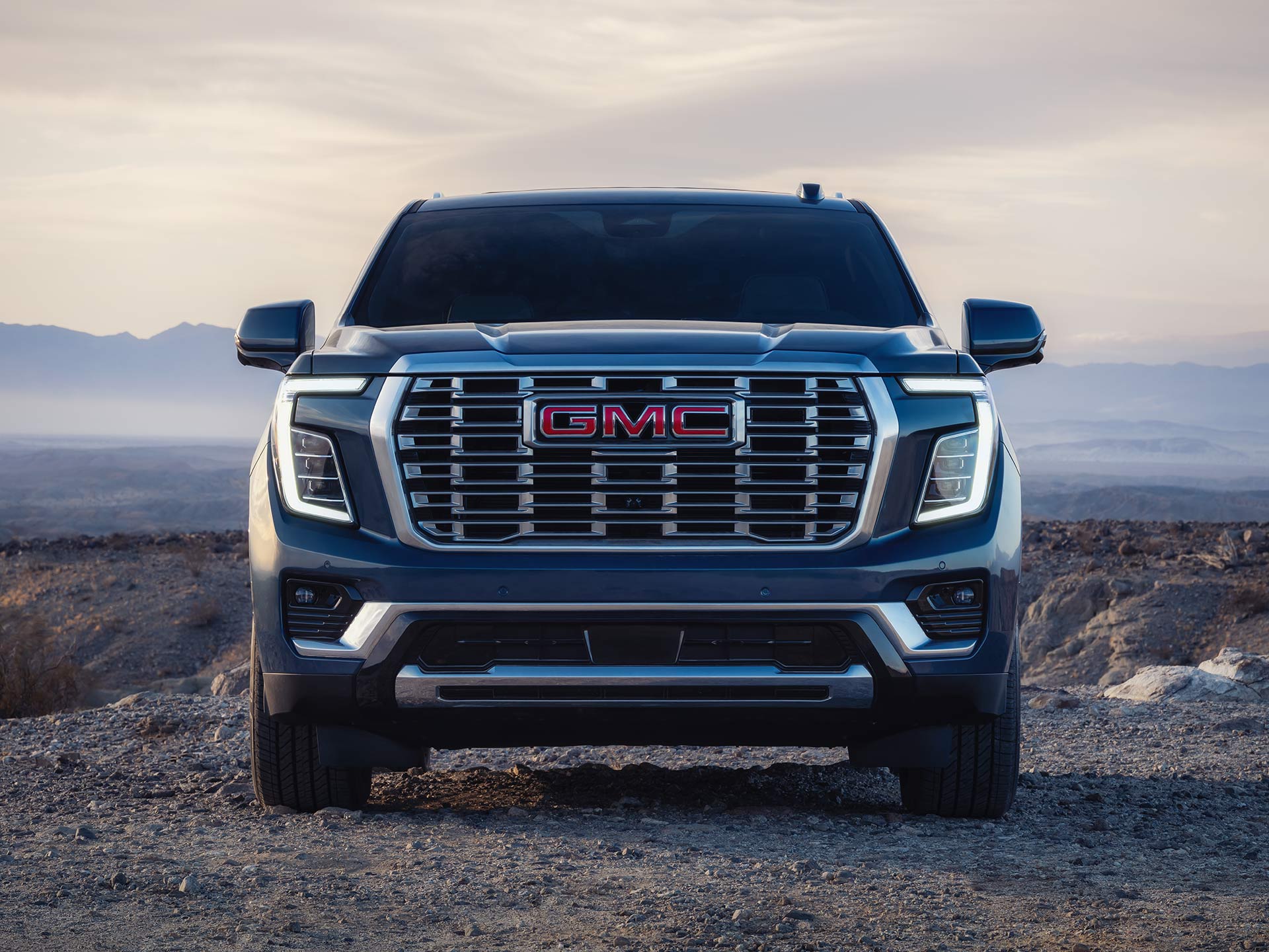 A Dark GMC Yukon with a Large Grille Parked on Rocky Ground in a Desert