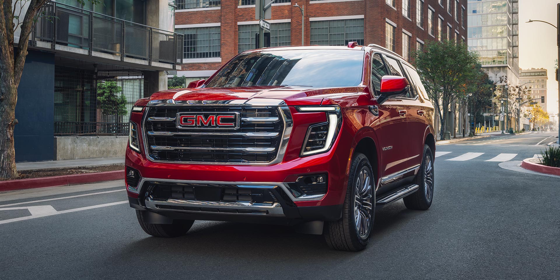 A Red GMC Yukon Driving on a City Street with Buildings in the Background