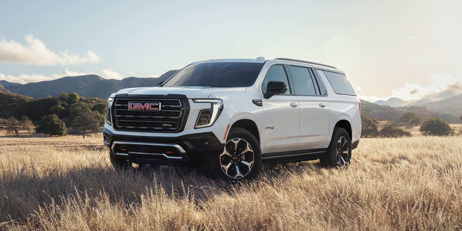 A White GMC Yukon AT4 Parked in a Field of Dry Grass under a Bright Sky
