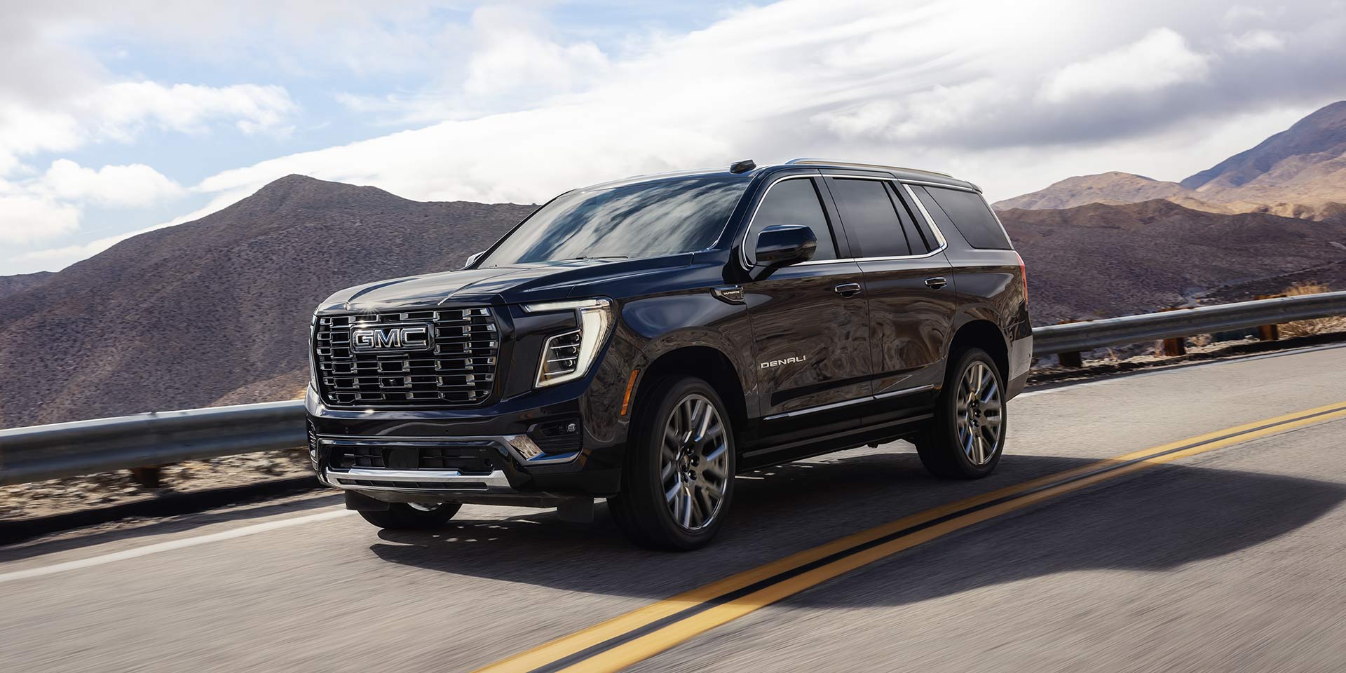 A Black GMC Yukon Denali Driving on a Winding Road with Mountains in the Background