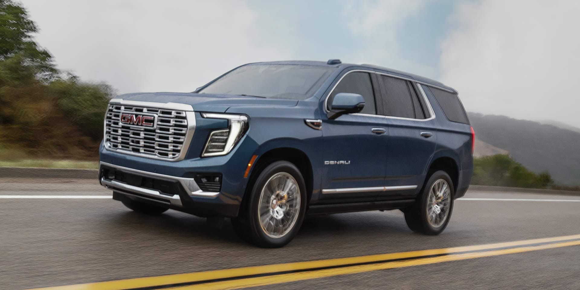 A Blue GMC Yukon Denali Driving on a Wet Road on a Cloudy Day
