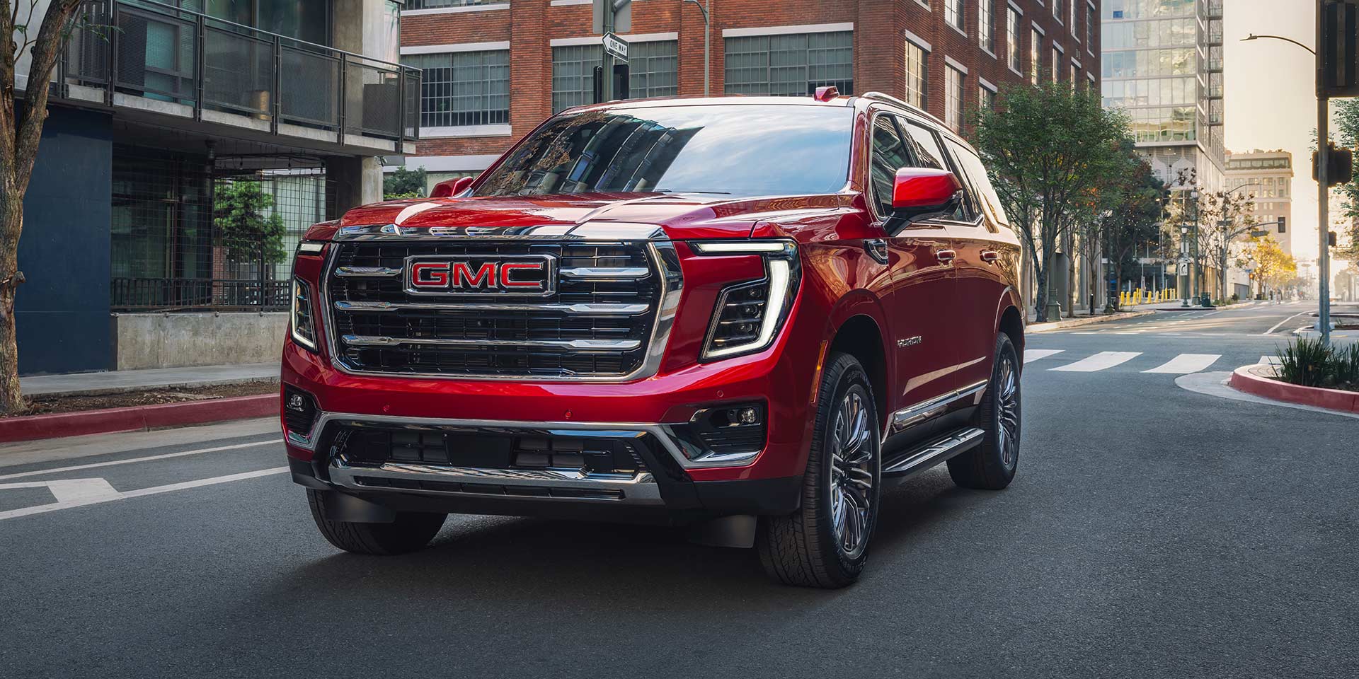 A Red GMC Yukon Driving on a City Street with Buildings in the Background