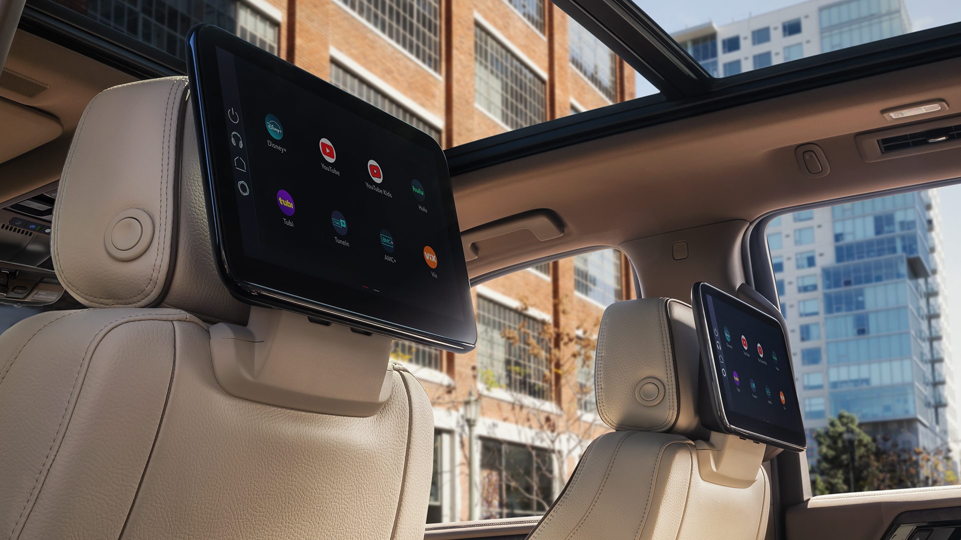 Rear Interior View of a GMC Yukon XL with Dual Seatback Screens and a Panoramic Sunroof in a City Setting
