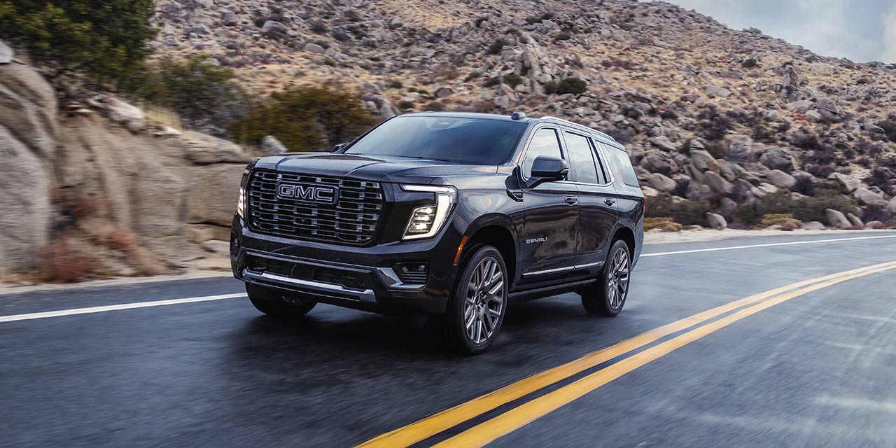 Dark Gray GMC Yukon Denali Ultimate SUV Driving on an Open Road Through a Rocky Mountain Landscape