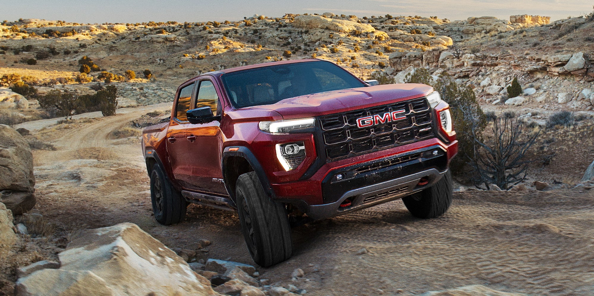 A Red 2027 GMC Canyon AT4X Pickup Truck Climbing a Rocky Dirt Hill From a Front Angle
