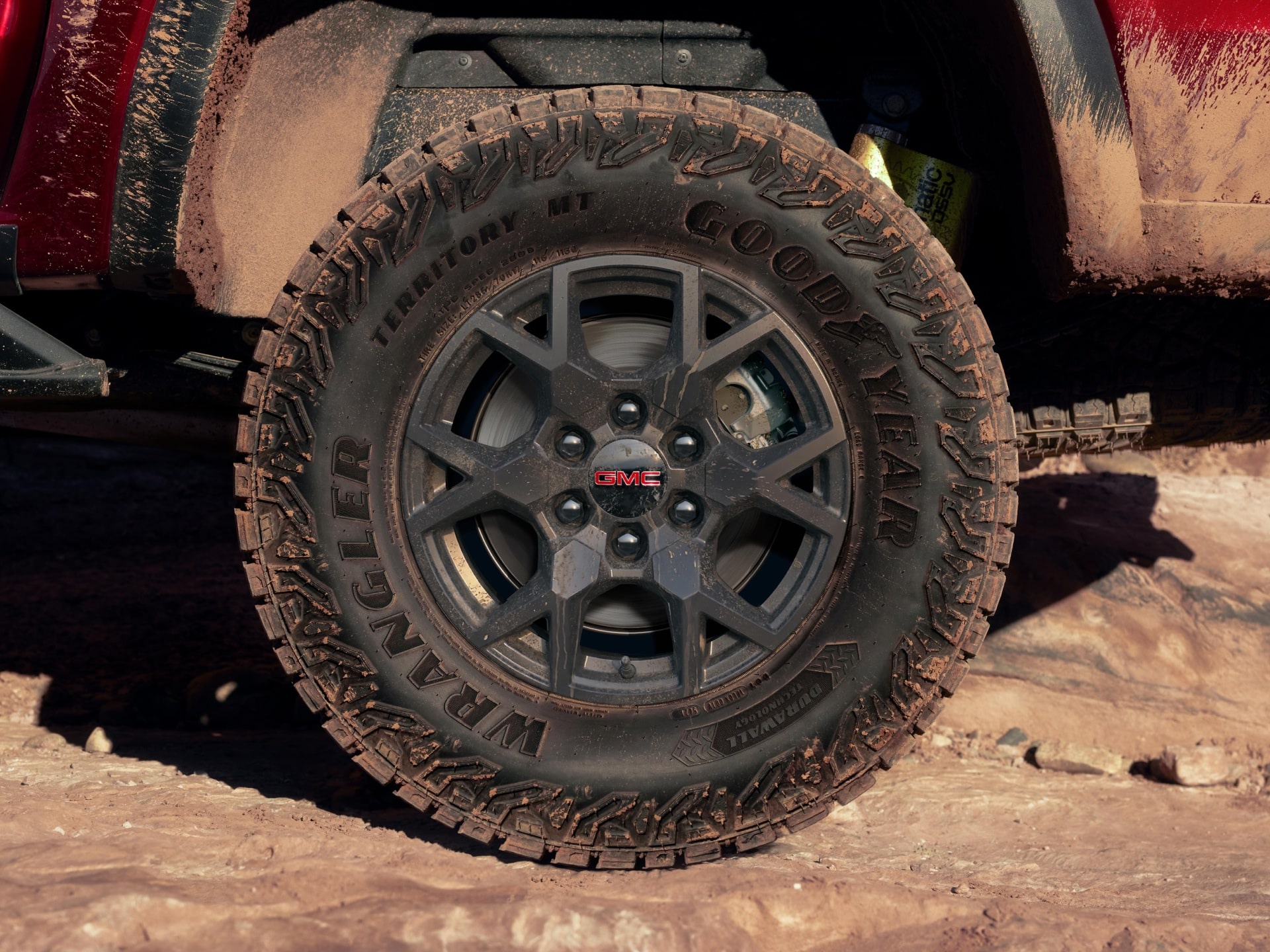 A Close-Up View of a Dirty Goodyear Wrangler Off-Road Tire on a Red 2027 GMC Canyon AT4X