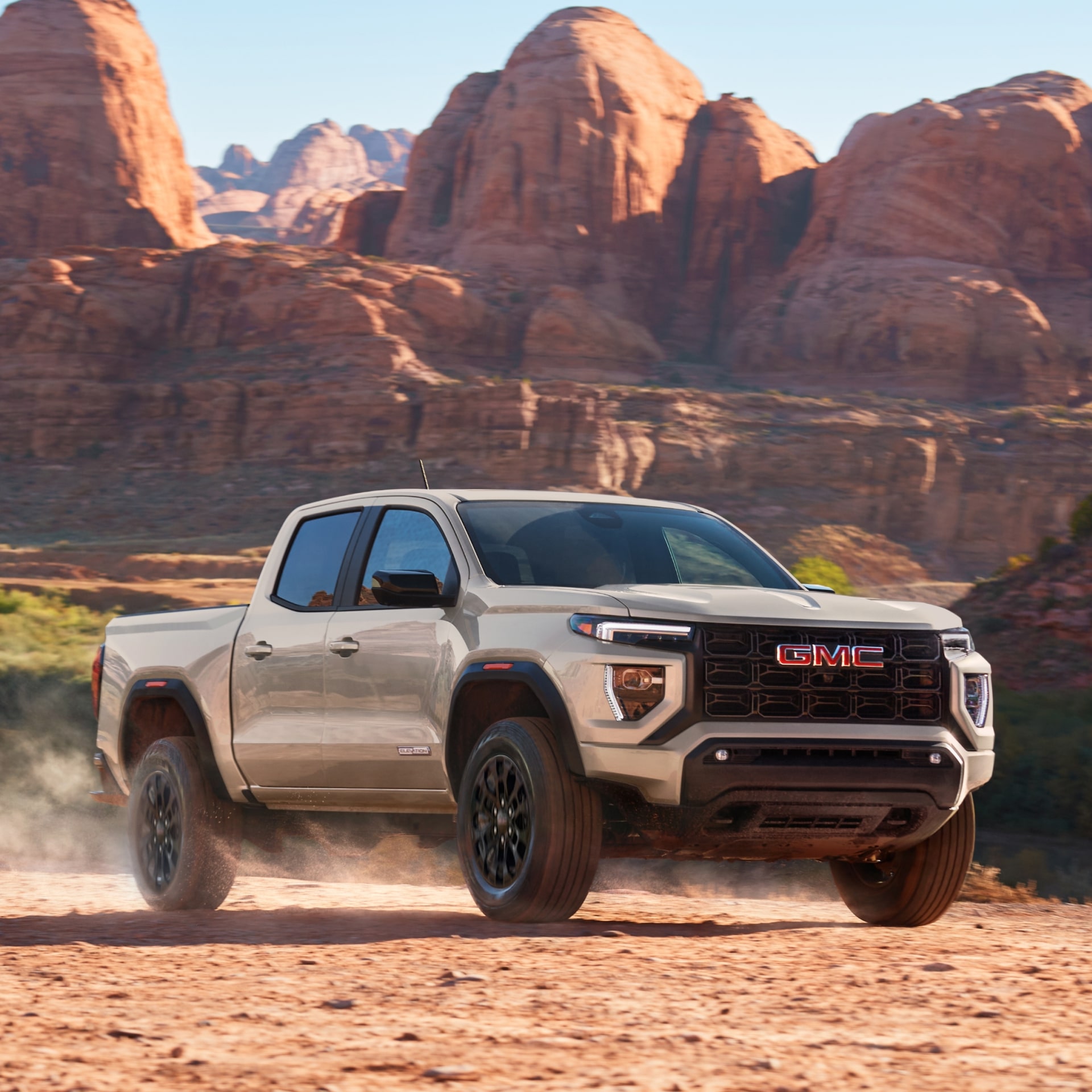 A White 2027 GMC Canyon AT4X Pickup Truck Parked on a Dirt Road with a Desert Mountain Range in the Background