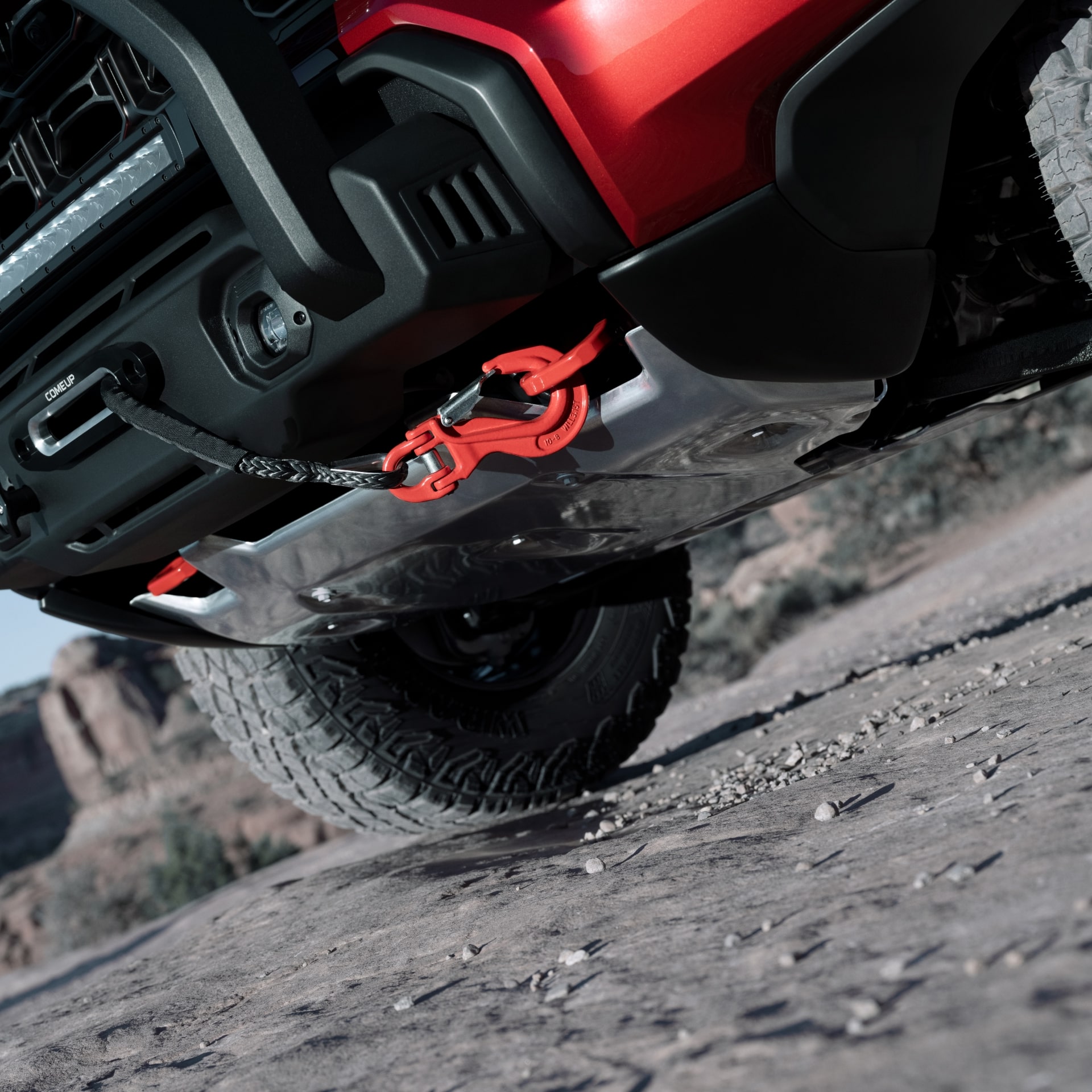 The Front Lower View of a Red 2027 GMC Canyon AT4X on a Rocky Trail with a Winch and Red Tow Hook