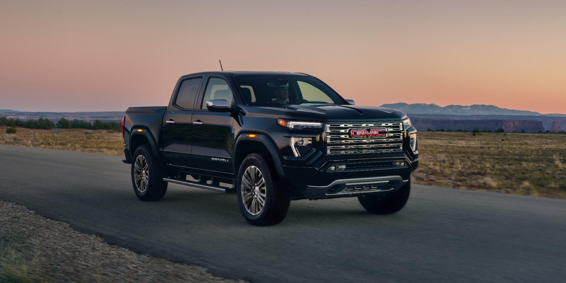 Side View Of a Black 2027 GMC Canyon Denali Truck Parked on a Paved Road With a Sunset Sky