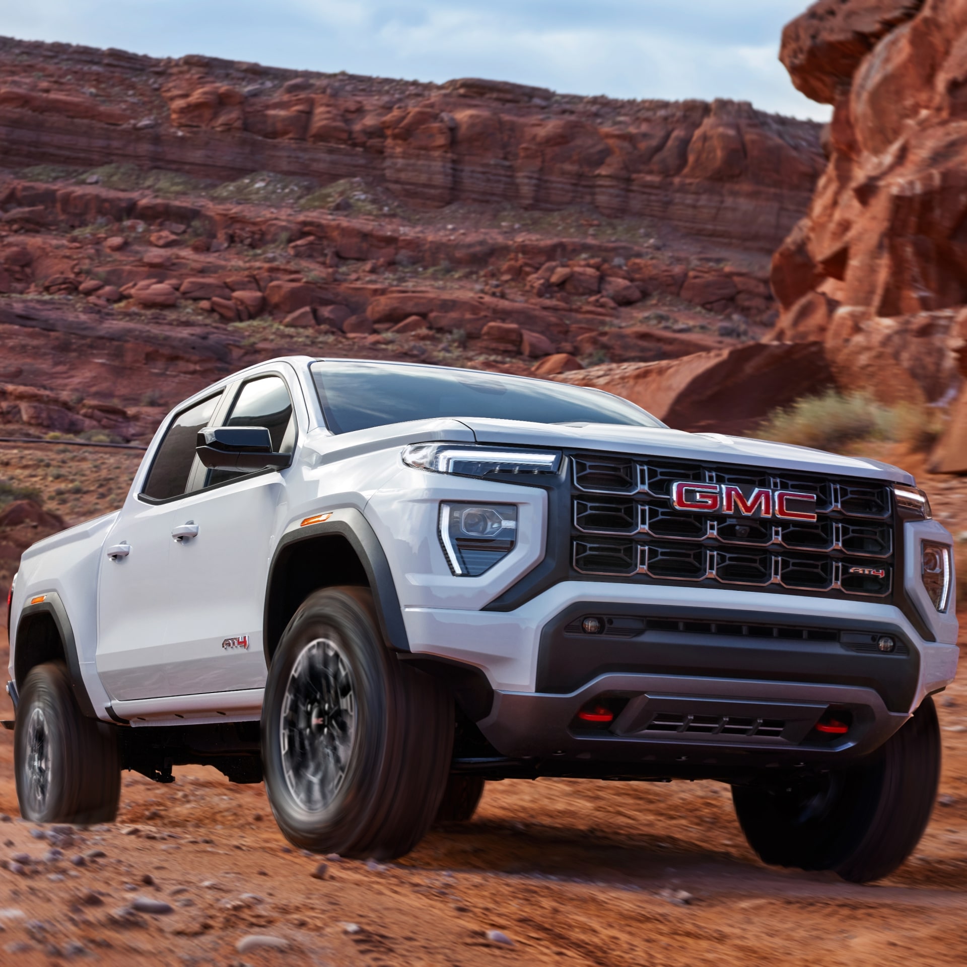 A White GMC Canyon AT4X Driving on a Dusty Rocky Desert Road with Red Rock Formations
