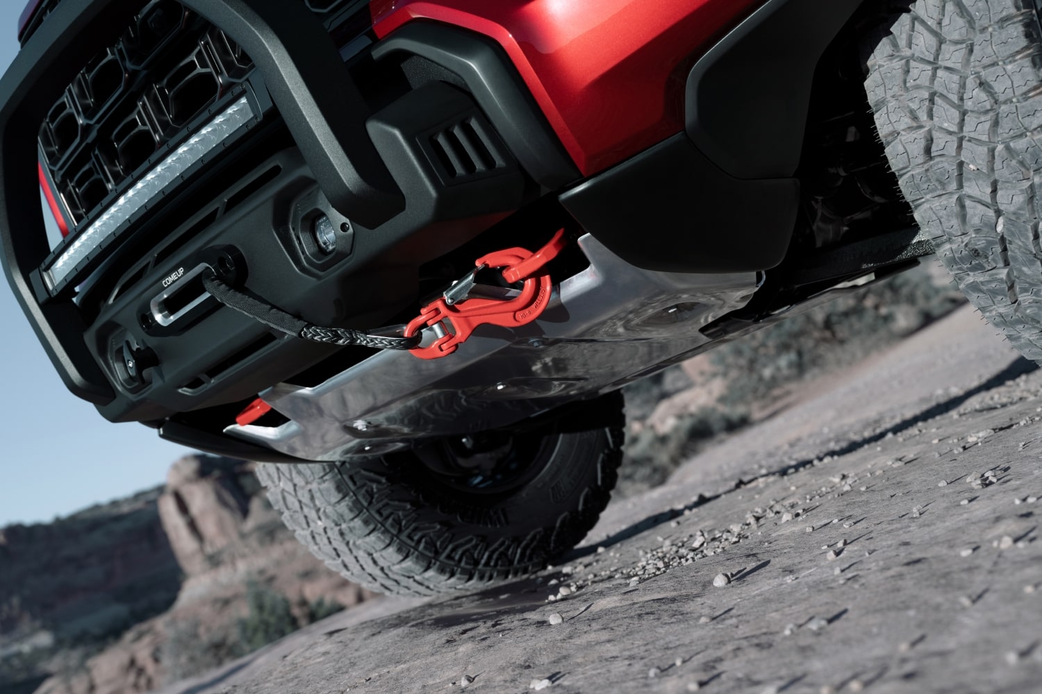 The Front Lower View of a Red 2027 GMC Canyon AT4X on a Rocky Trail with a Winch and Red Tow Hook