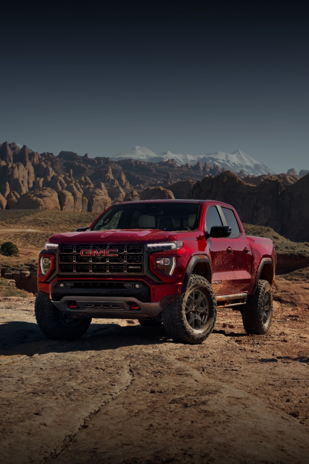 A Red 2027 GMC Canyon AT4X Parked in a Grassy Field with Mountains in the Background