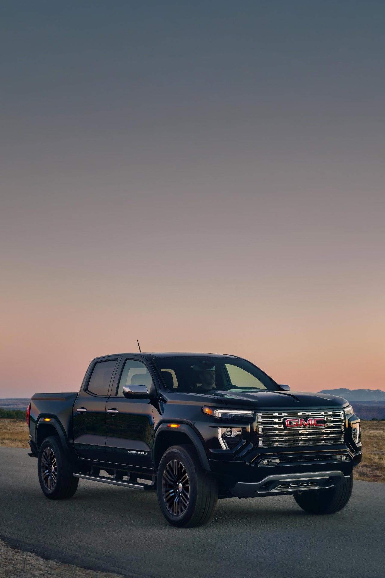Side View Of a Black 2027 GMC Canyon Denali Truck Parked on a Paved Road With a Sunset Sky