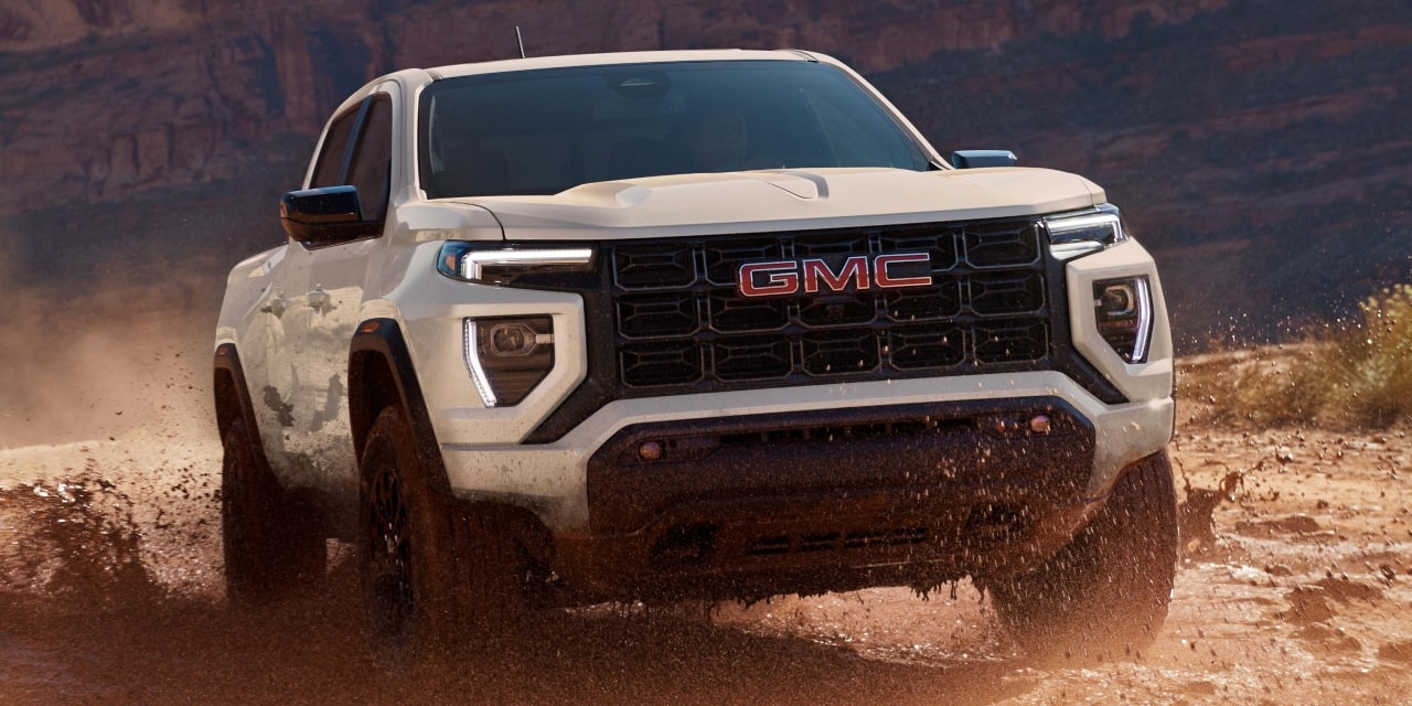 Front View Of a White 2027 GMC Canyon AT4X Truck Splashing Through Mud on an Off-Road Trail
