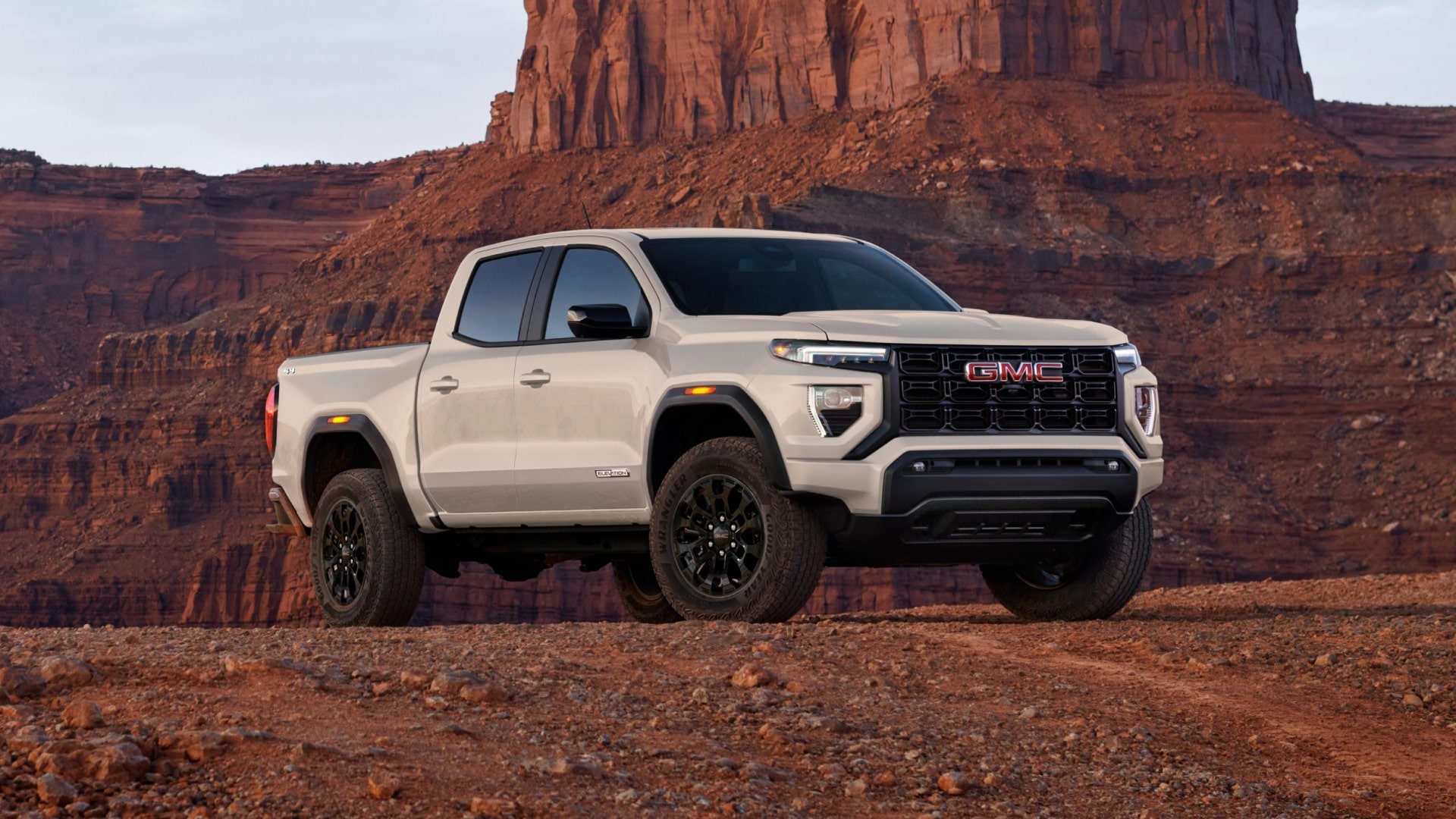 A Summit White 2027 GMC Canyon AT4X Truck Parked on a Rocky Desert Terrain With Large Rock Formations