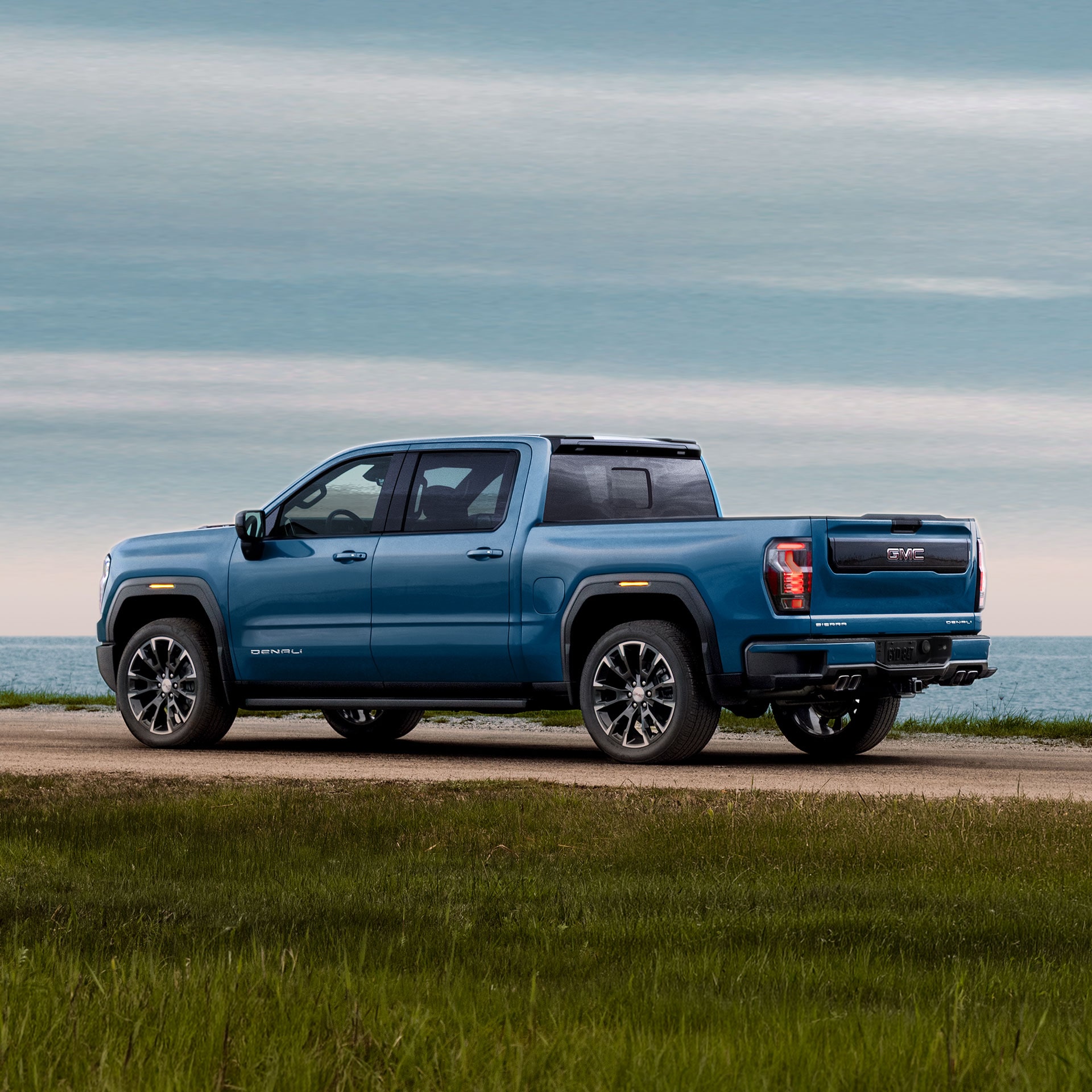 A Side View of a Blue GMC Sierra 1500 Denali Parked on a Grassy Dirt Road by the Ocean