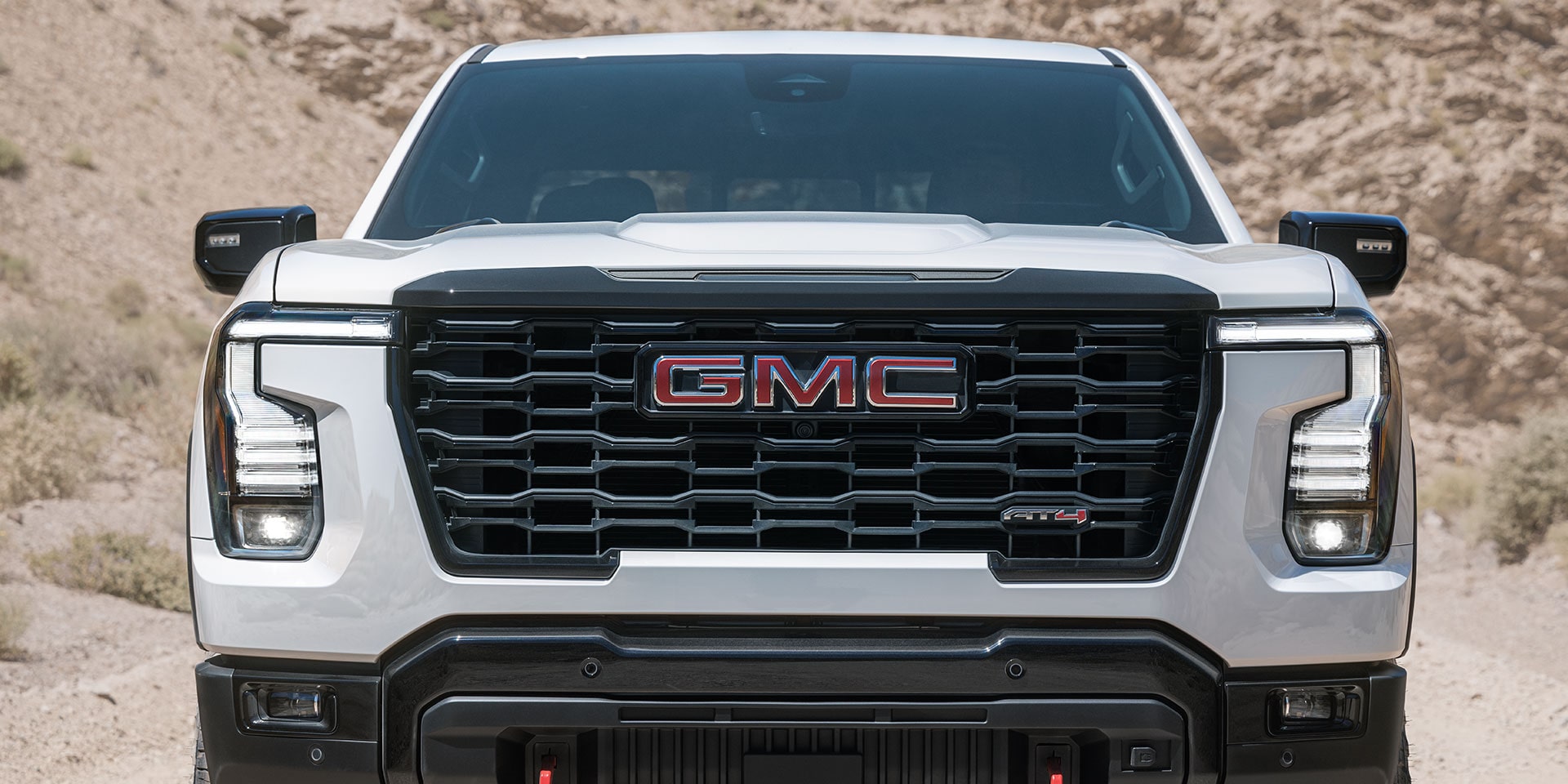 The Front View of a White GMC Sierra 1500 AT4X Truck With a Red GMC Logo on the Grille