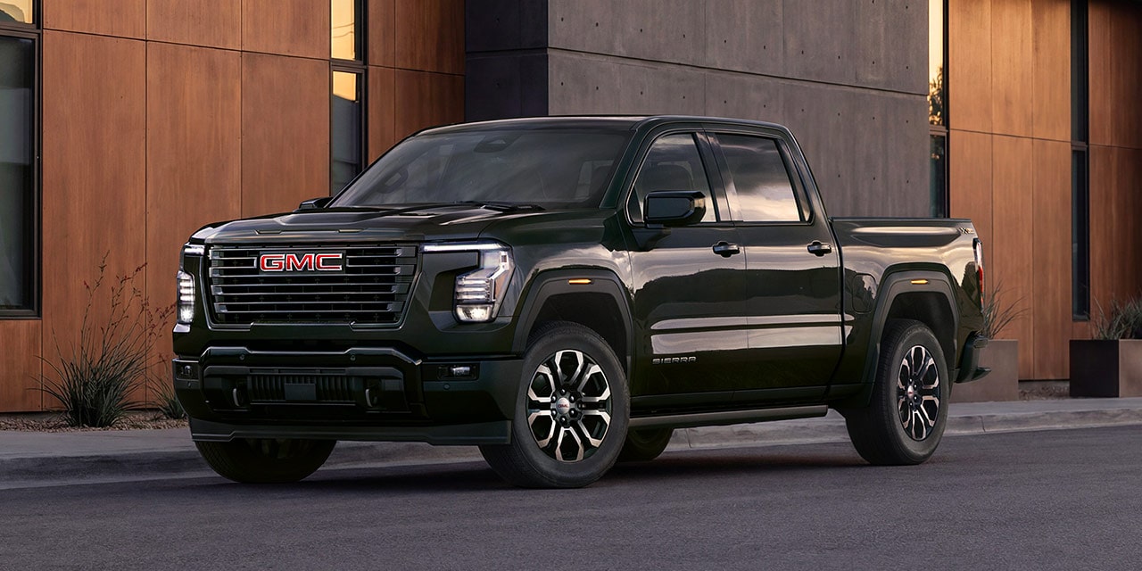 A Front 3/4 View of a Dark Metallic Green GMC Sierra 1500 Parked in front of a Modern Building