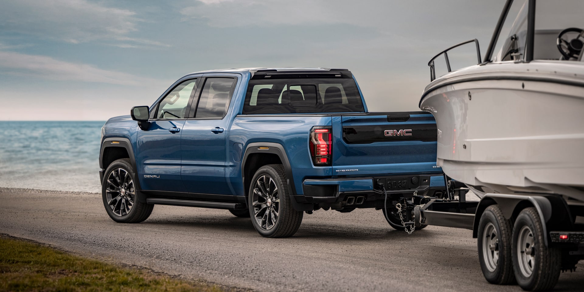 2027 GMC Sierra 1500 Denali towing a boat on a seaside road