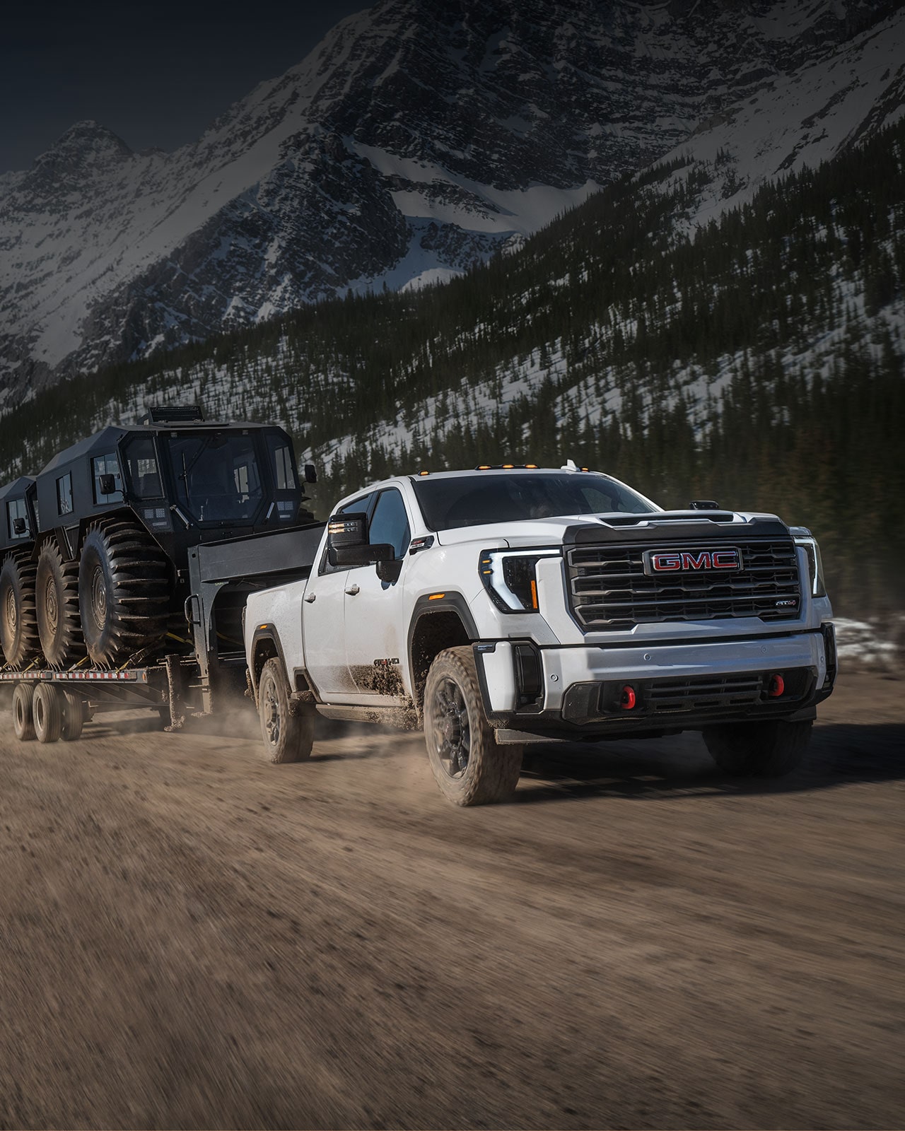 A Red GMC Sierra HD AT4X Truck Pulling a Trailer and Off-Roading in a Rocky Desert with Mountains