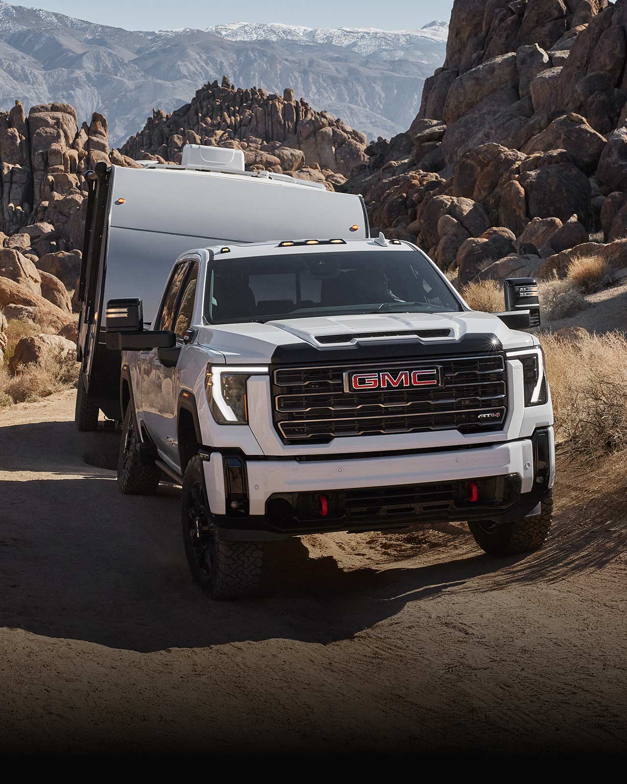 A White 2027 GMC Sierra HD AT4X Pulling a White Trailer on a Rocky Dirt Road