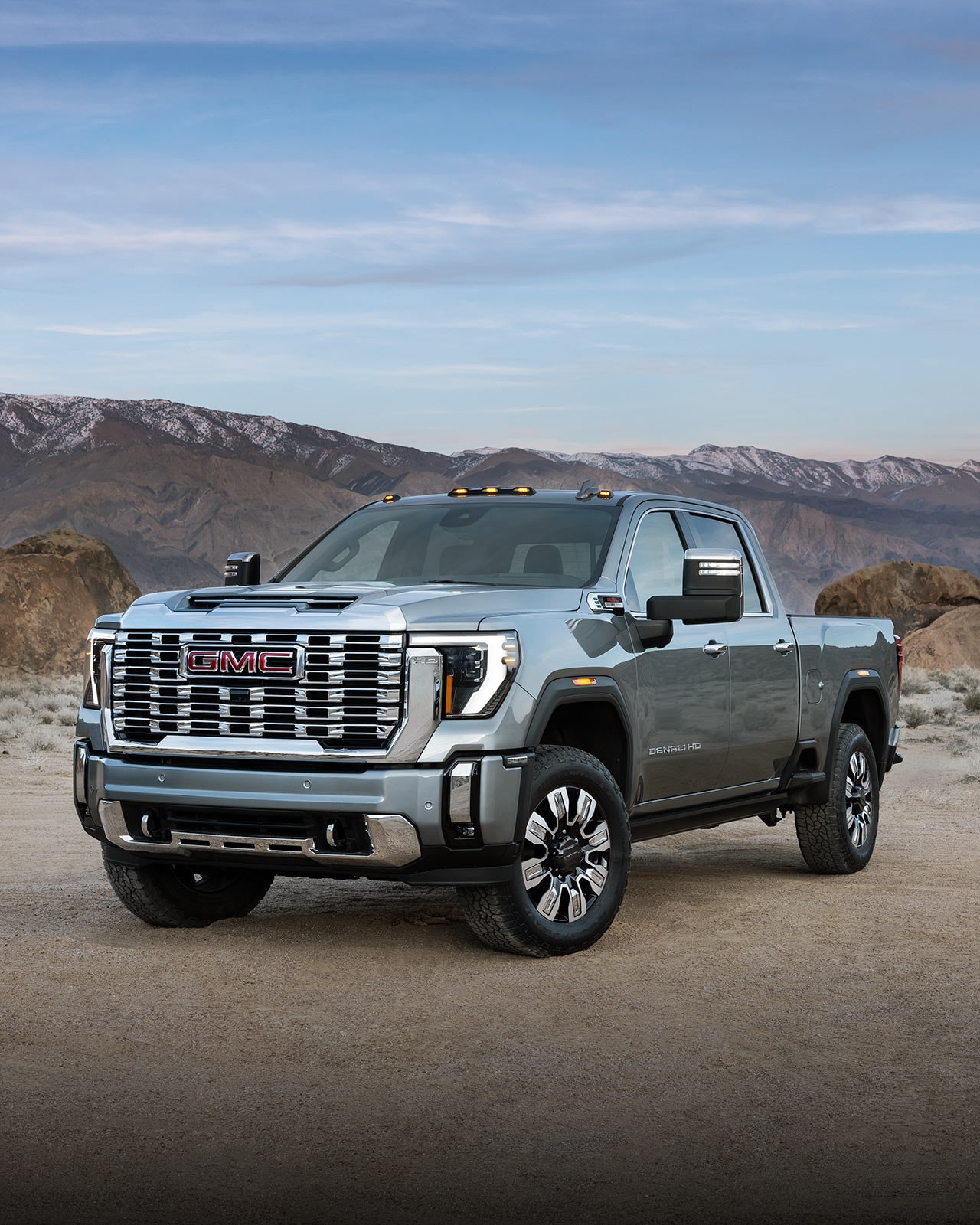 A Front View of a Gray GMC Sierra HD Denali Pickup Truck Parked on a Dirt Road with Mountains