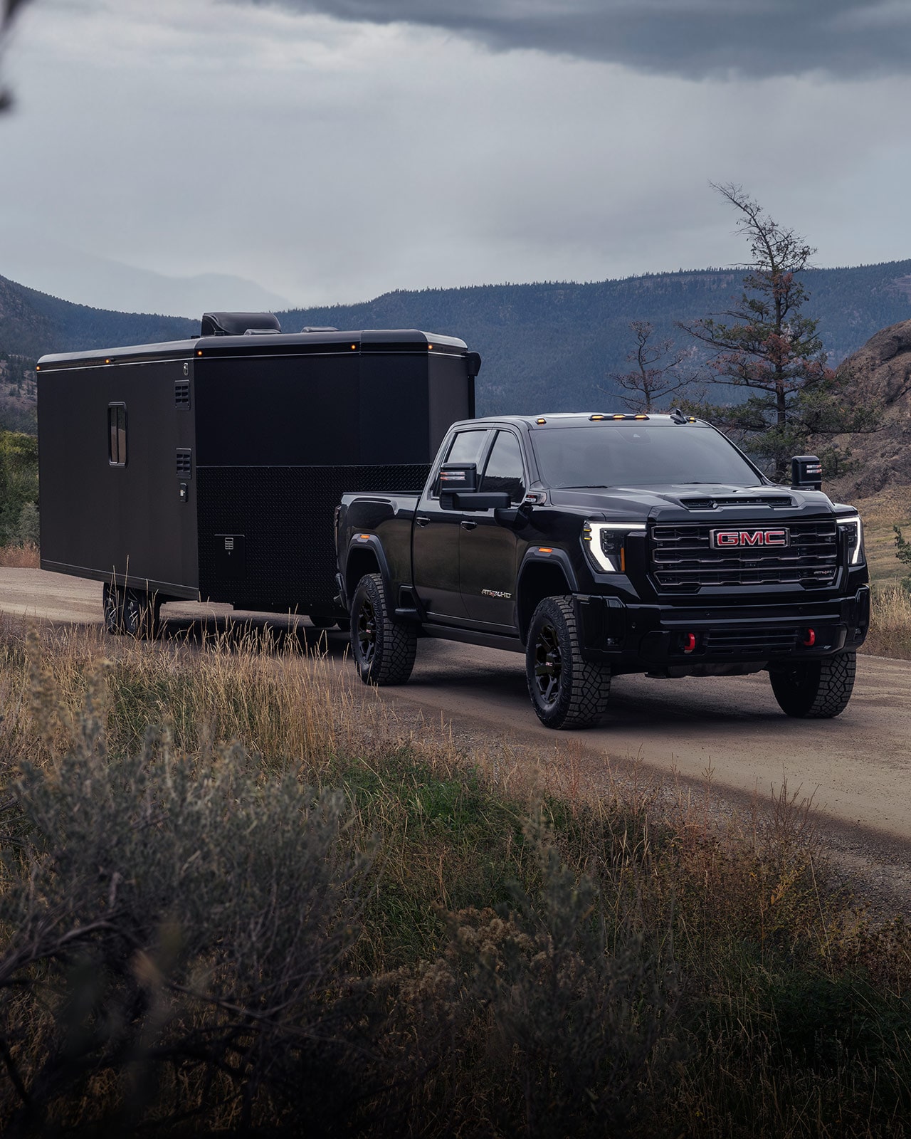 A Black GMC Sierra HD AT4X Truck Pulling a Large Box Trailer on a Dirt Road
