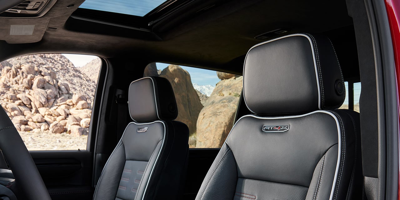 The Interior of a GMC Sierra HD AT4X Truck Showing Black Leather Seats with a Sunroof and Rocky Landscape