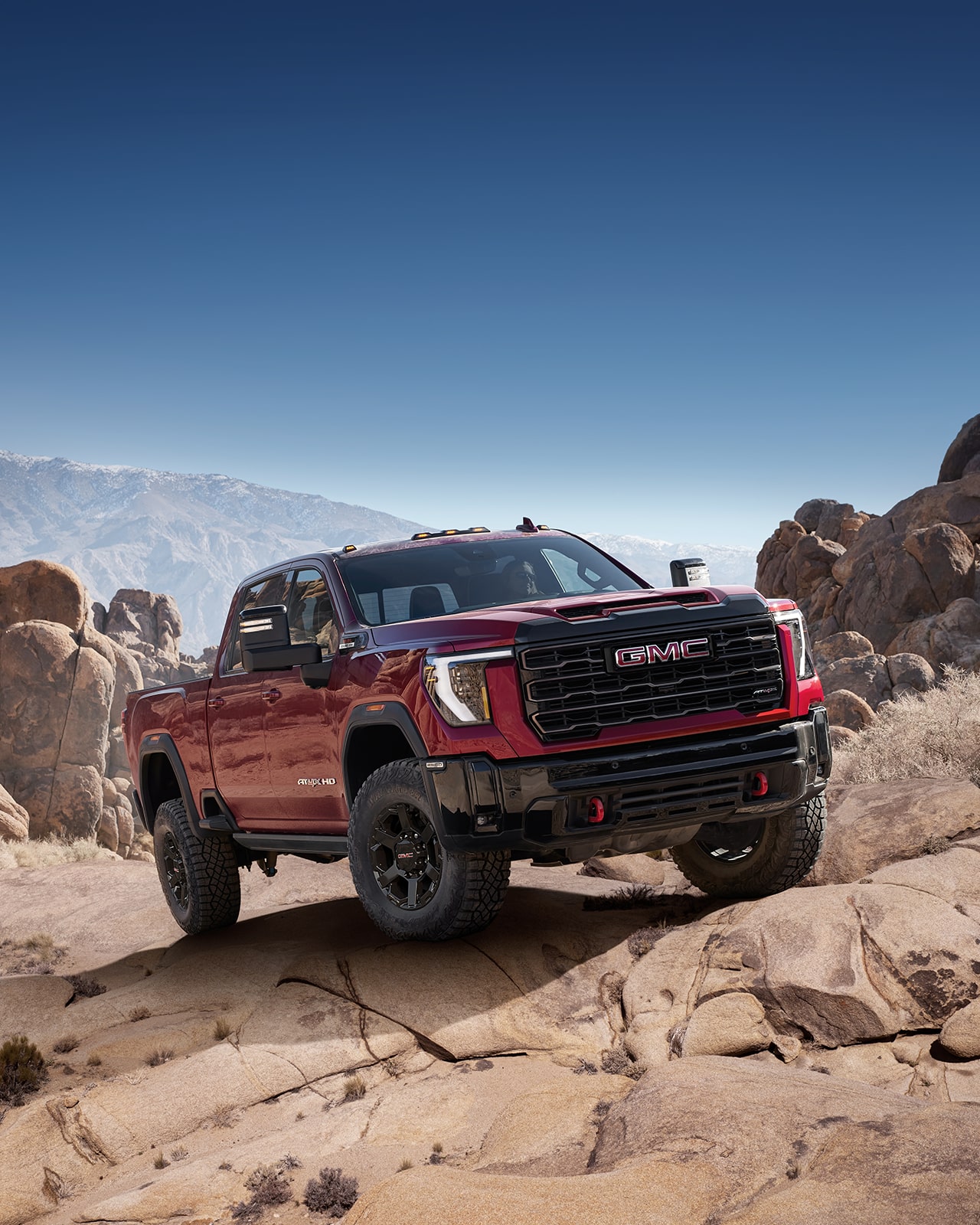 A Red 2027 GMC Sierra HD AT4X Driving through a Rocky Desert Landscape