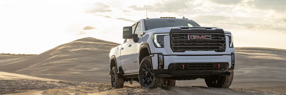 The All White GMC Sierra HD AT4 Driving Uphill on Sand with a Sunset