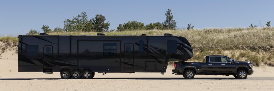 The New GMC Sierra HD in Black Driving On-Road Pulling a large Trailer