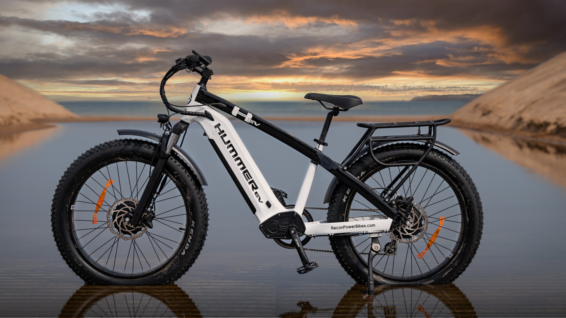 Side View of the AWD Electric Bike Parked on the Beach in a Puddle of Water with a Colorful Sunset View in the Background