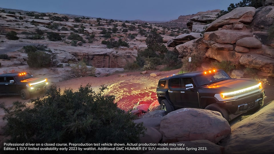Two GMC HUMMERS EV Driving Through a Canyon at Twilight with Their Lights on