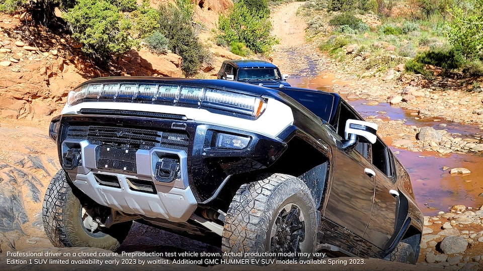Three-Quarters Front View of the GMC HUMMER EV Driving up a Steep Incline with a Small Pool of Water on the Trial Behind the Vehicle