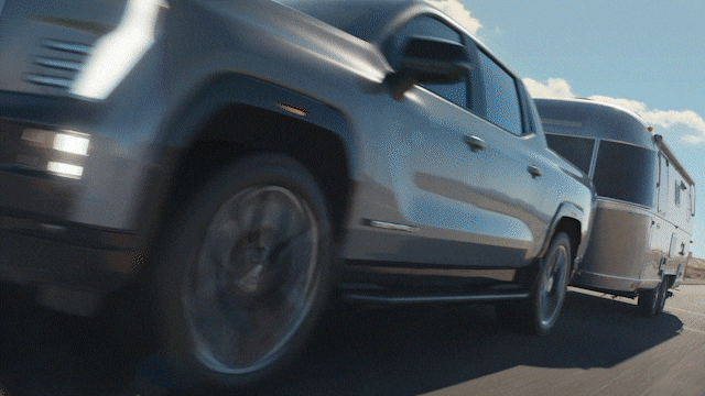 A GIF that is Displaying the New GMC Sierra EV Denali Driving On-Road Towing a Trailer