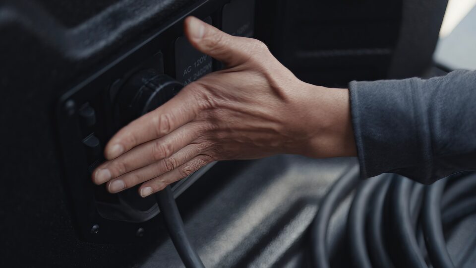 A Persons hand on the Electric Charging Port of the GMC Sierra EV with Text Overlay saying "Mobile Power Station