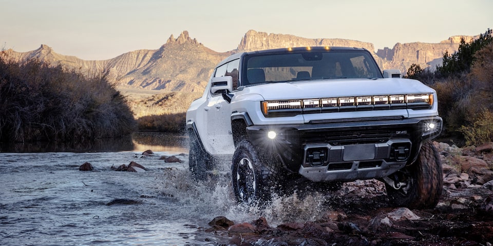 The Hummer EV Pickup Crossing a Stream of Water While Off-Roading in the Mountains 