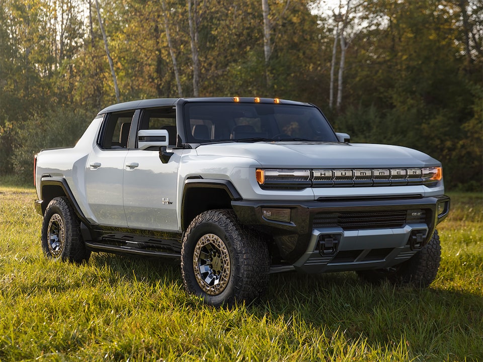 The Hummer EV Pickup Parked in a Grass Field with a Forest Backdrop