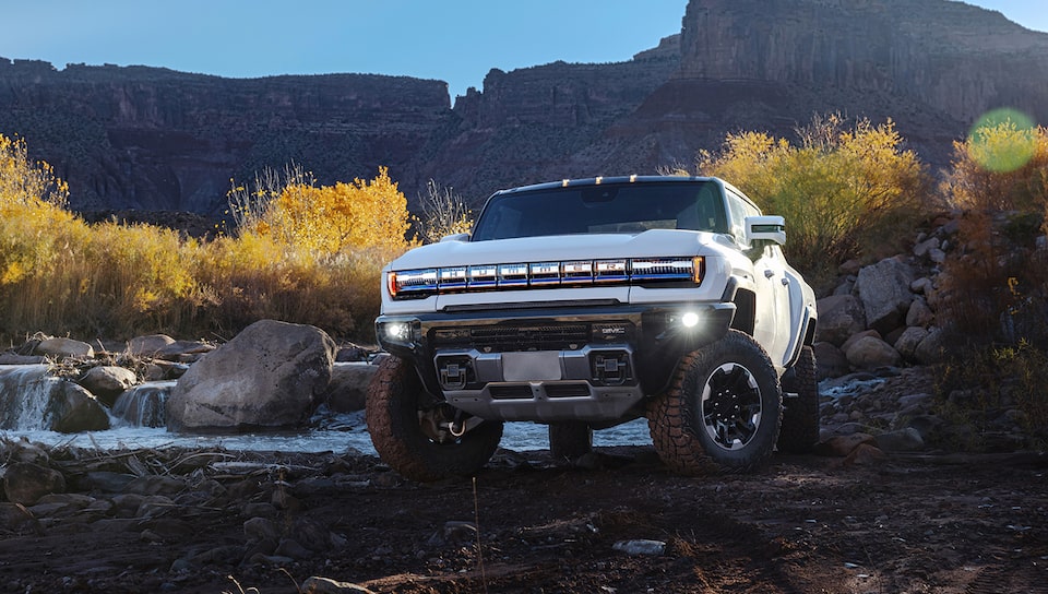 The Hummer EV Pickup Truck Parked Off-Road Next to a Stream with a Moutain Backdrop 