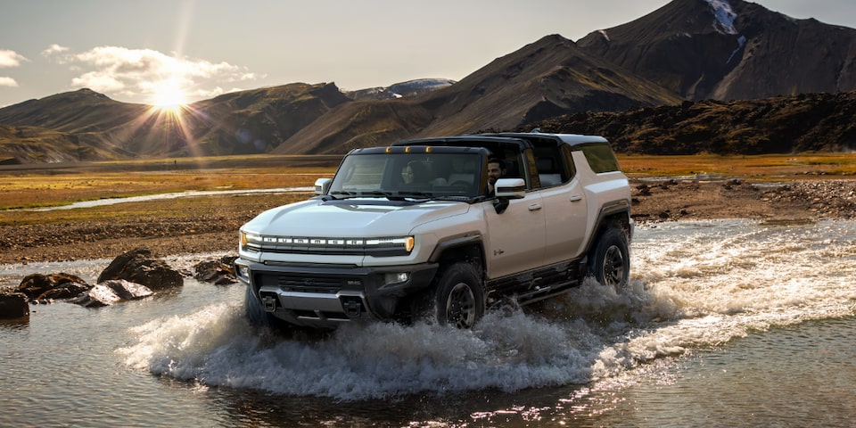 The Hummer EV Off-Roading in a Body of Water with a Mountain Backdrop 