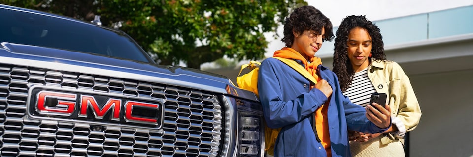Two People Standing Next to the Front of a GMC Vehicle