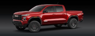 A Red GMC Canyon Elevation Pickup Truck Is Parked From a Front Three-Quarters Angle Against a Dark Background