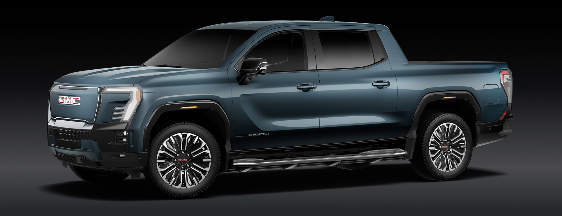 A Blue GMC Sierra EV Denali Electric Pickup Truck Is Parked From a Front Three-Quarters Angle Against a Dark Background