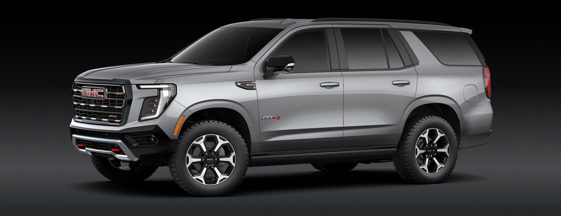 A Sterling Metallic GMC Yukon Denali SUV Is Parked From a Front Three-Quarters Angle Against a Dark Background