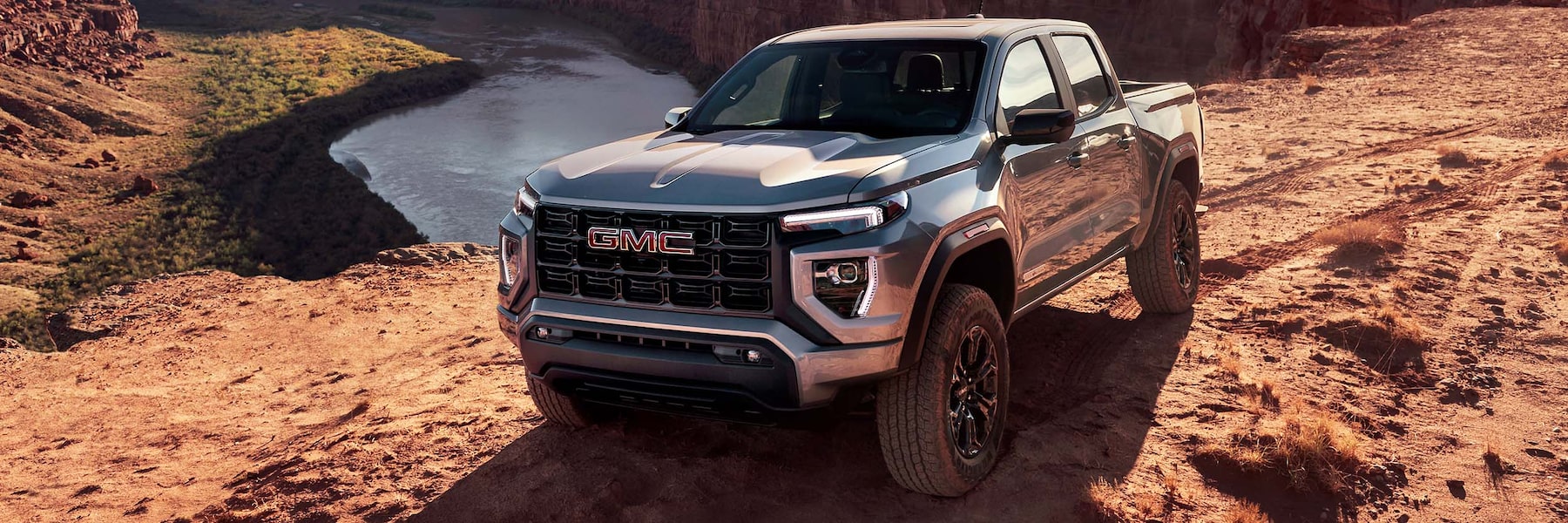  2024 GMC Canyon Elevation in Sterling Metallic driving on rugged dirt landscape. 