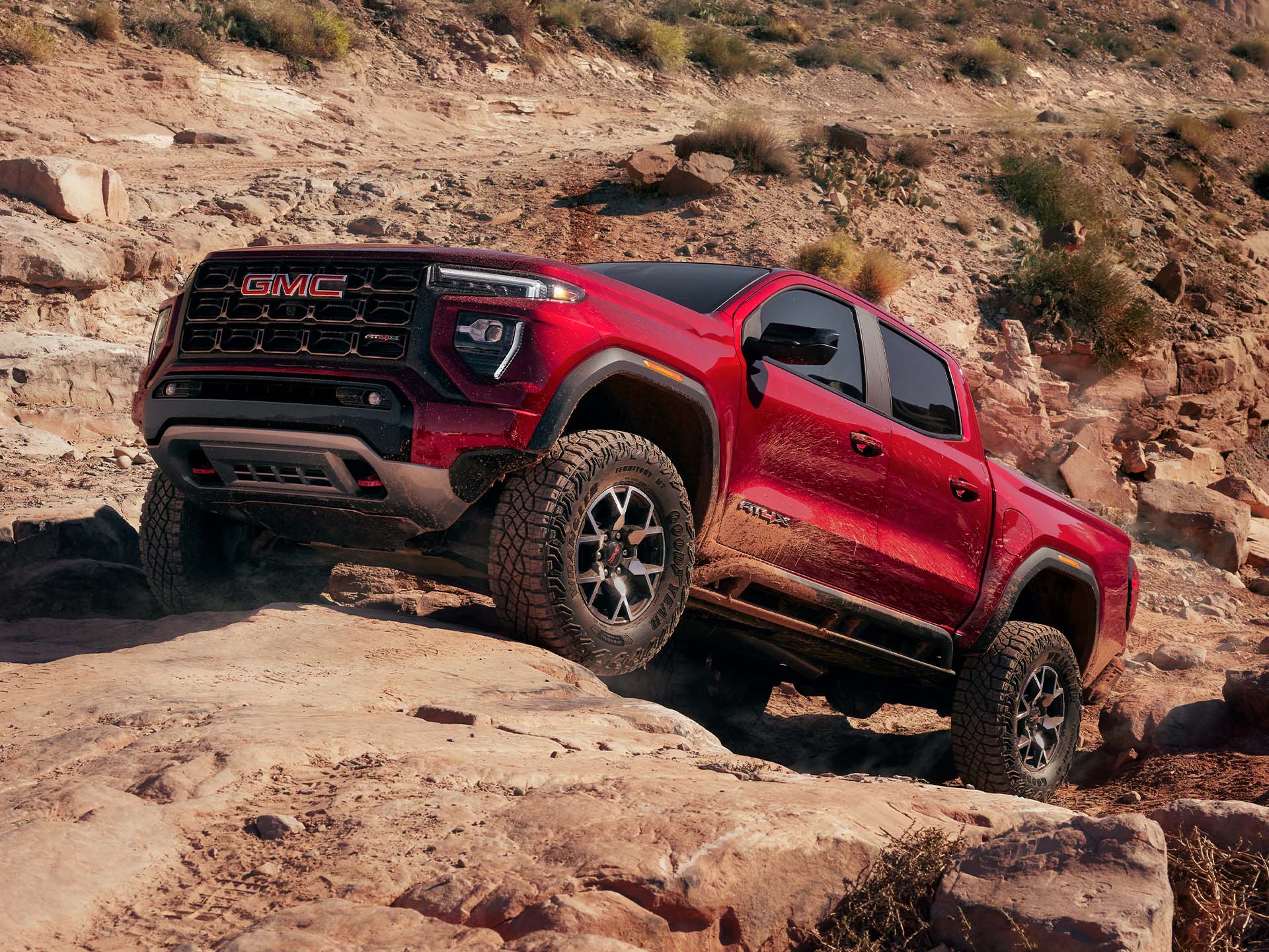  2024 GMC Canyon AT4X in Volcanic Red Tintcoat driving over large rocks. 
