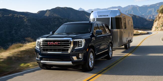 2024 Black 5.3L V8 SLT GMC Yukon towing an airstream on a country road