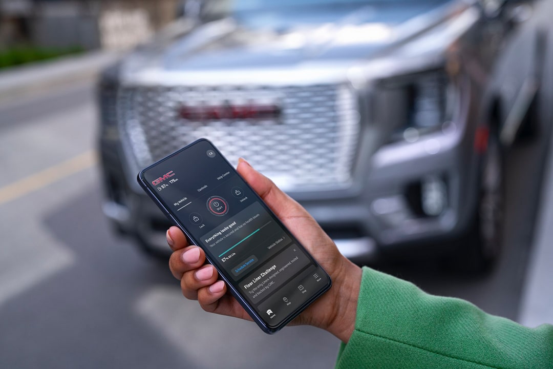 Close-up of a Smartphone Displaying the myGMC App with a GMC Vehicle Parked in the Background